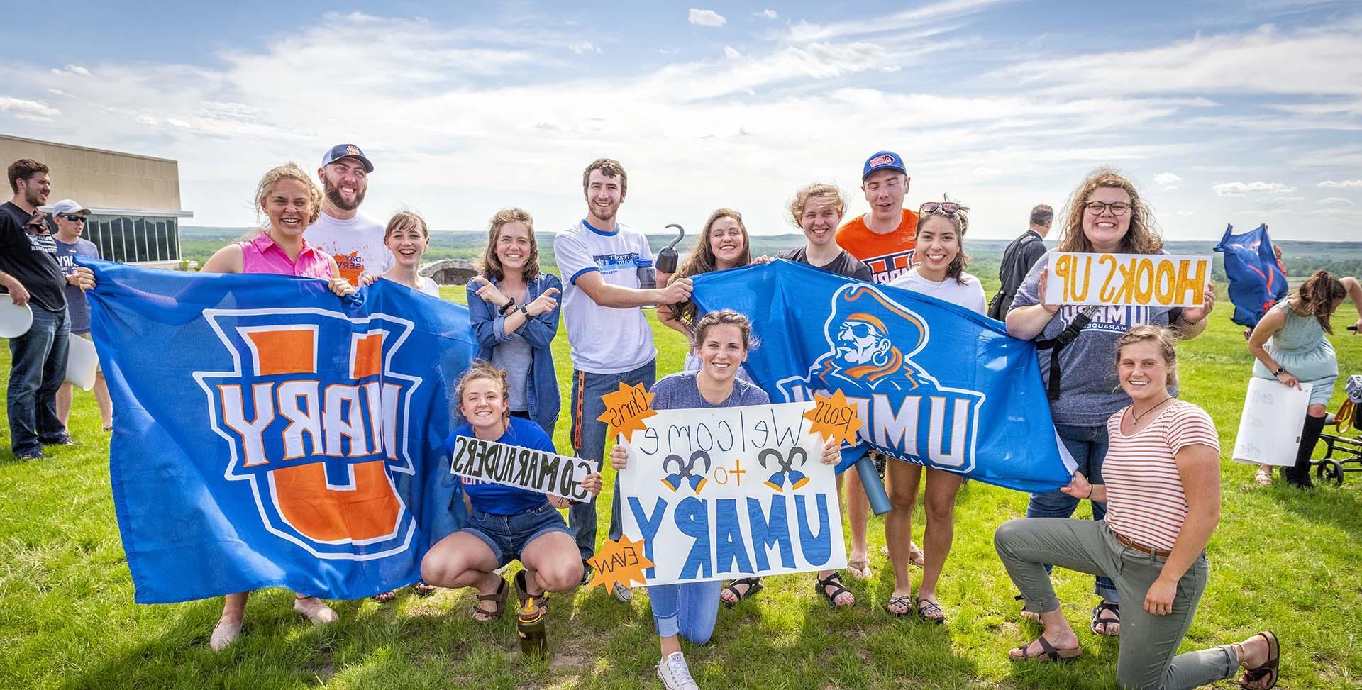 Students smiling holding up welcome signs and UMary flags.